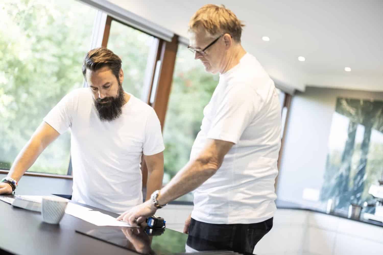 To håndværkere i hvide t-shirts i et køkken under renovering
